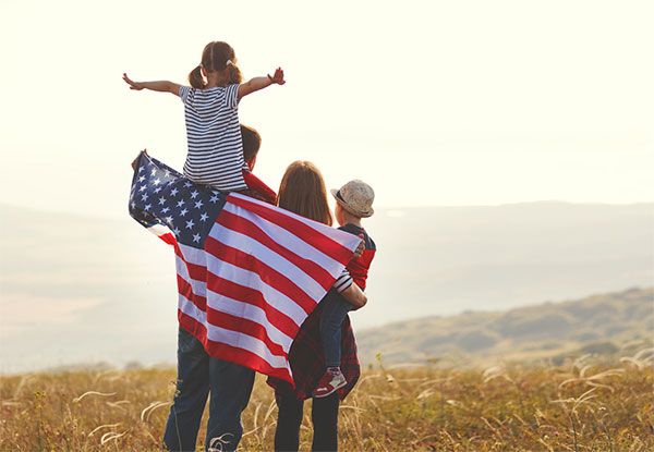 Young family standing on a hill outside looking at the horizon and holding an American flag.